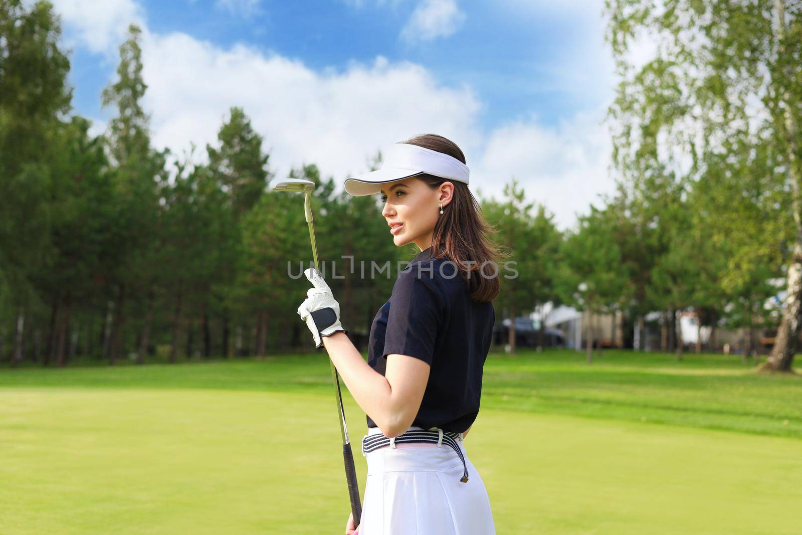 Professional female golfer holding golf club on field and looking away. Young woman standing on golf course on a sunny day.