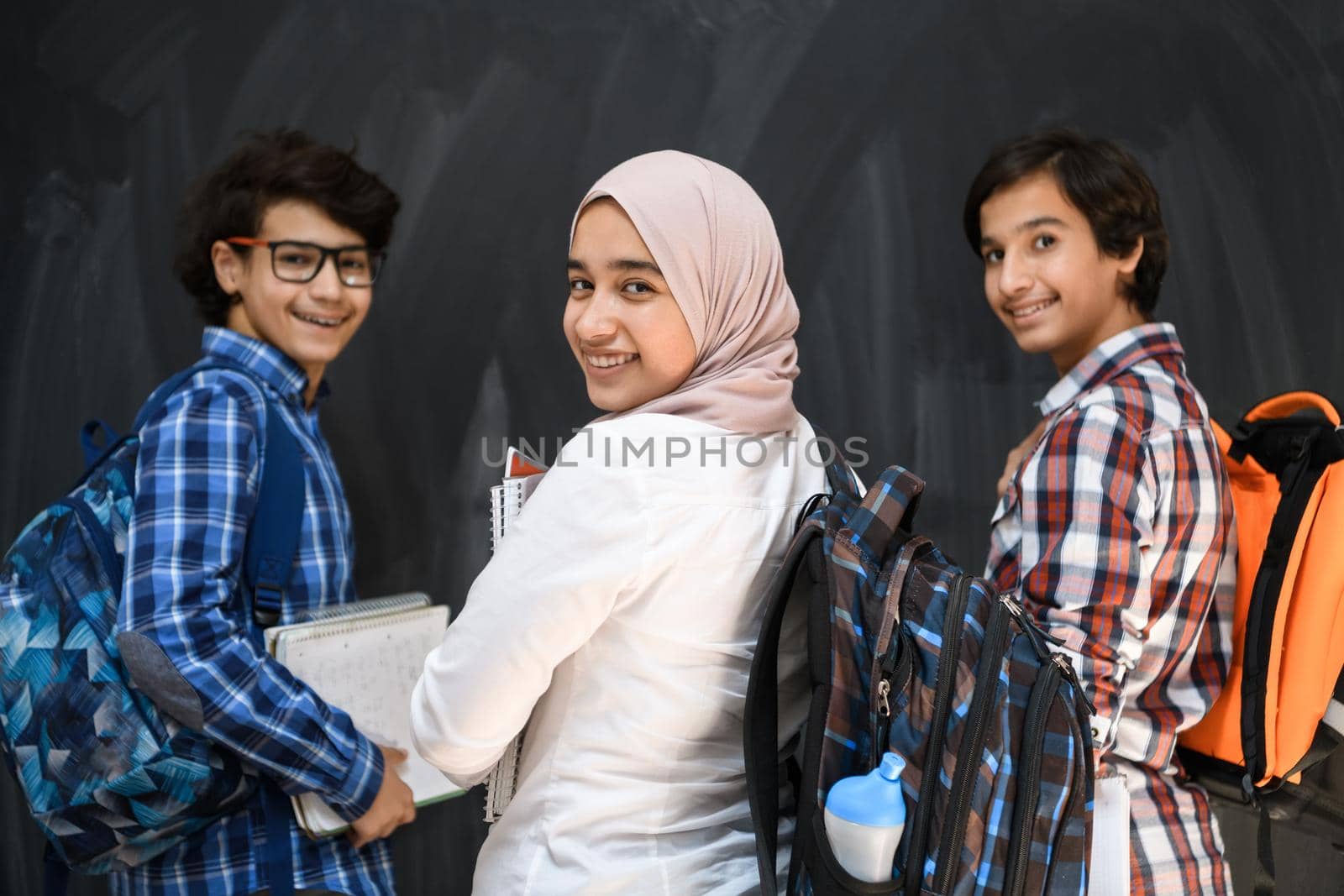 Arabic teenagers, students group portrait against black chalkboard wearing backpack and books in school.Selective focus. High quality photo