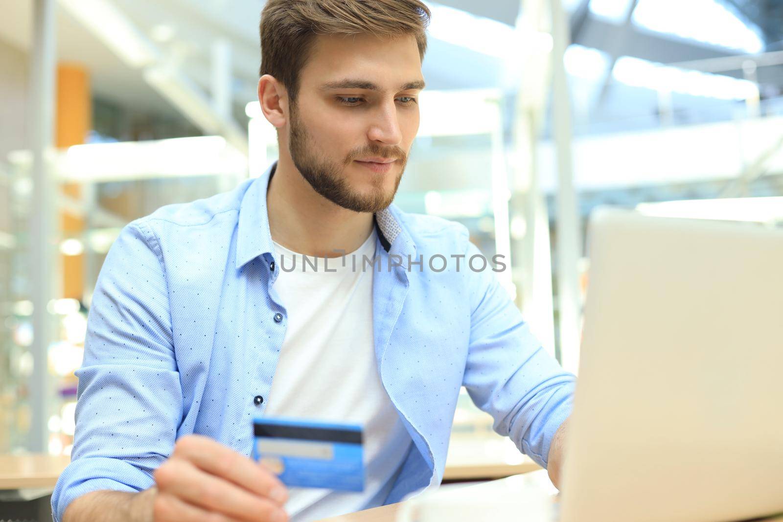 Smiling man sitting in office and pays by credit card with his laptop