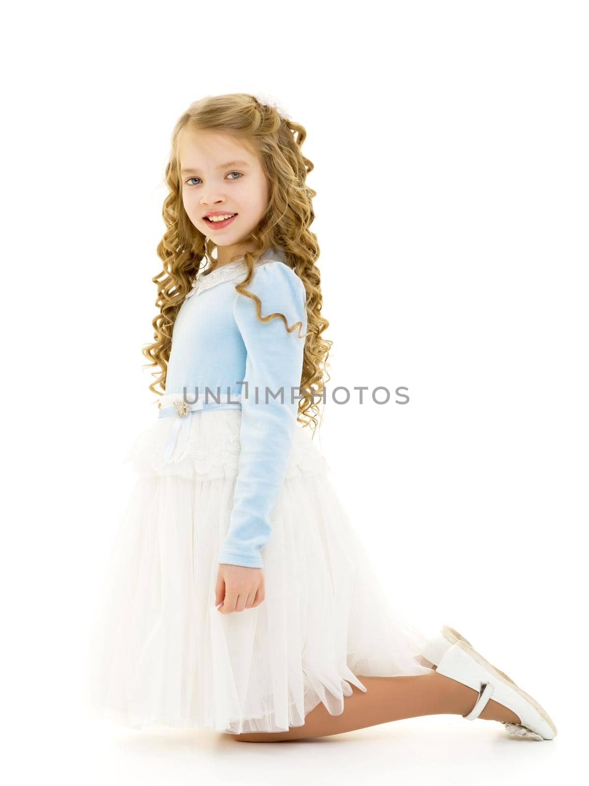 Beautiful little girl kneels in the studio on a white background. The concept of beauty and fashion, children's emotions. Isolated.