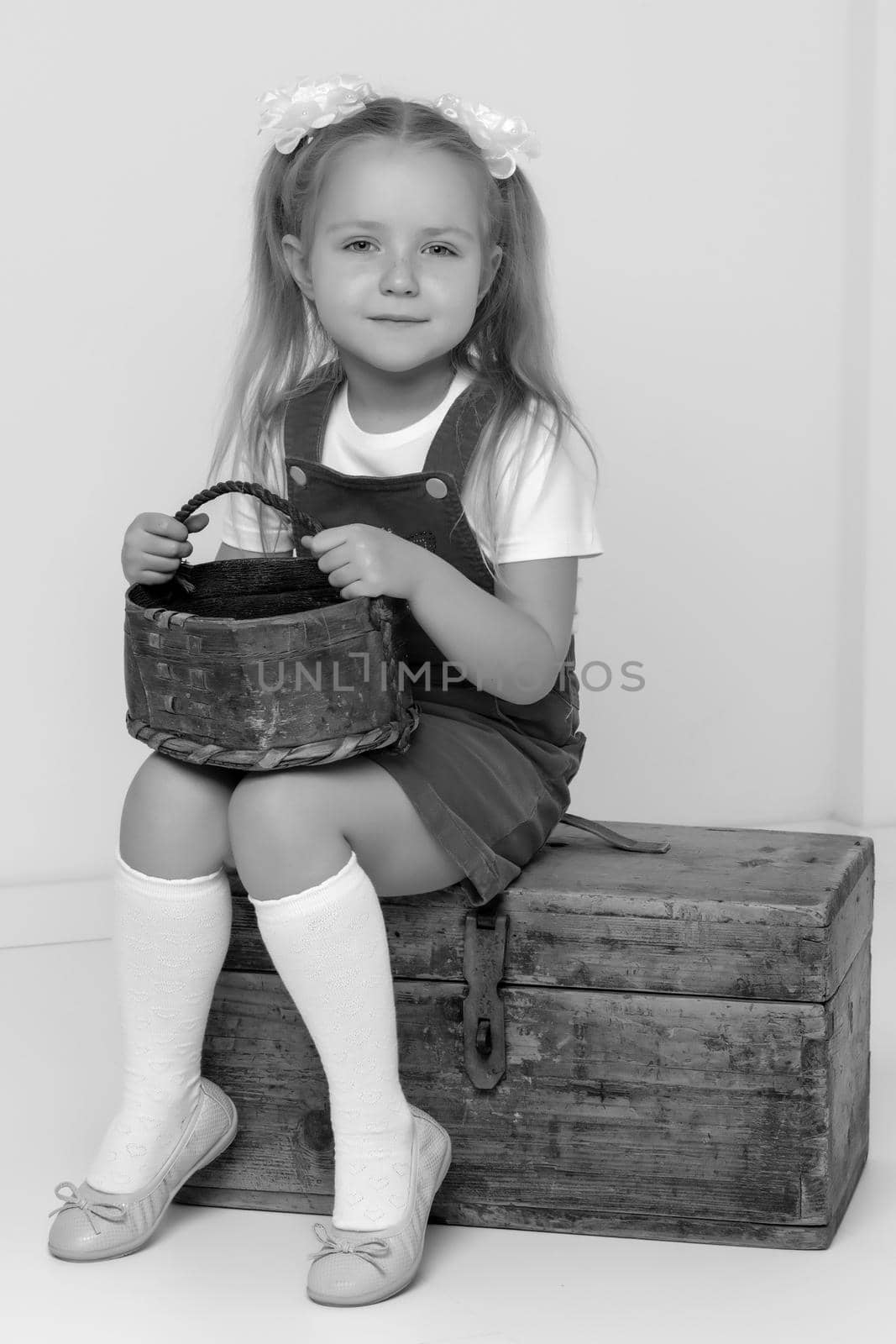 A little girl is sitting on an old suitcase with a basket in her hands. Retro style.