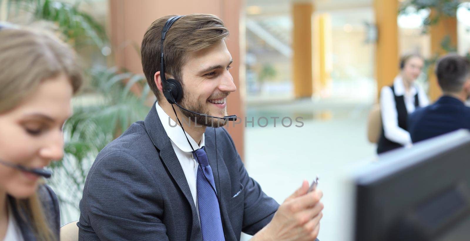 Portrait of call center worker accompanied by his team. Smiling customer support operator at work