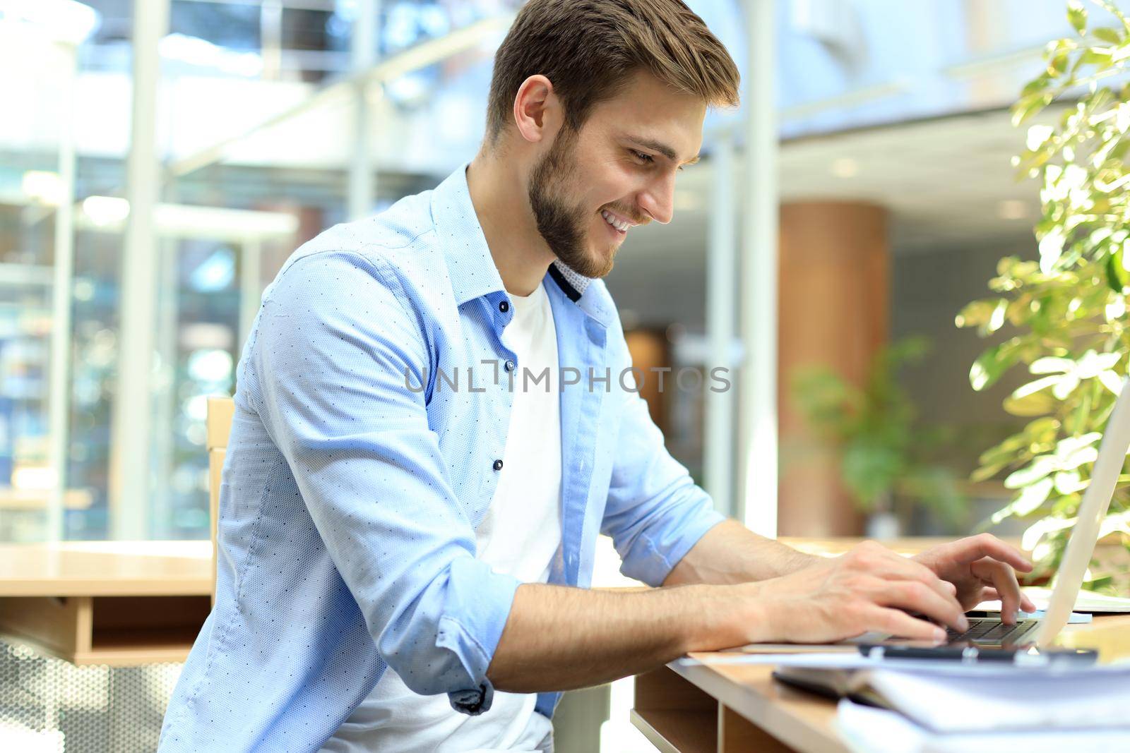 Portrait of young man sitting at his desk in the office and typing on the laptop