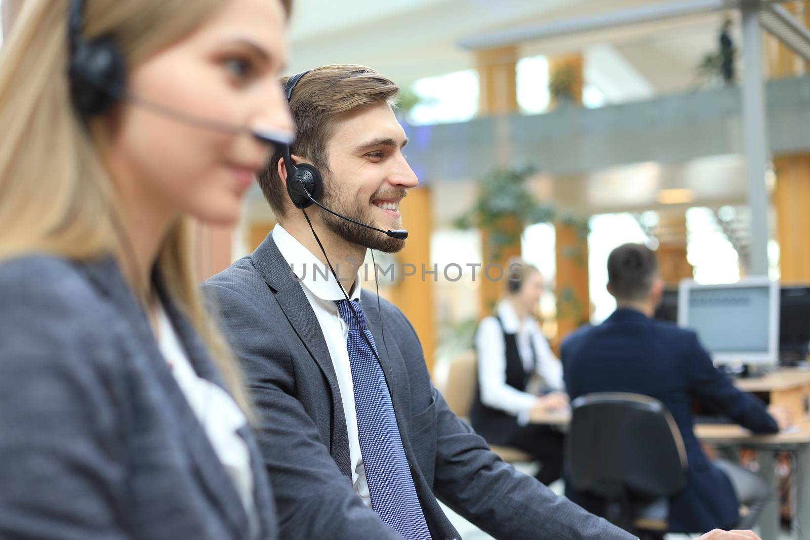 Portrait of call center worker accompanied by his team. Smiling customer support operator at work. by tsyhun