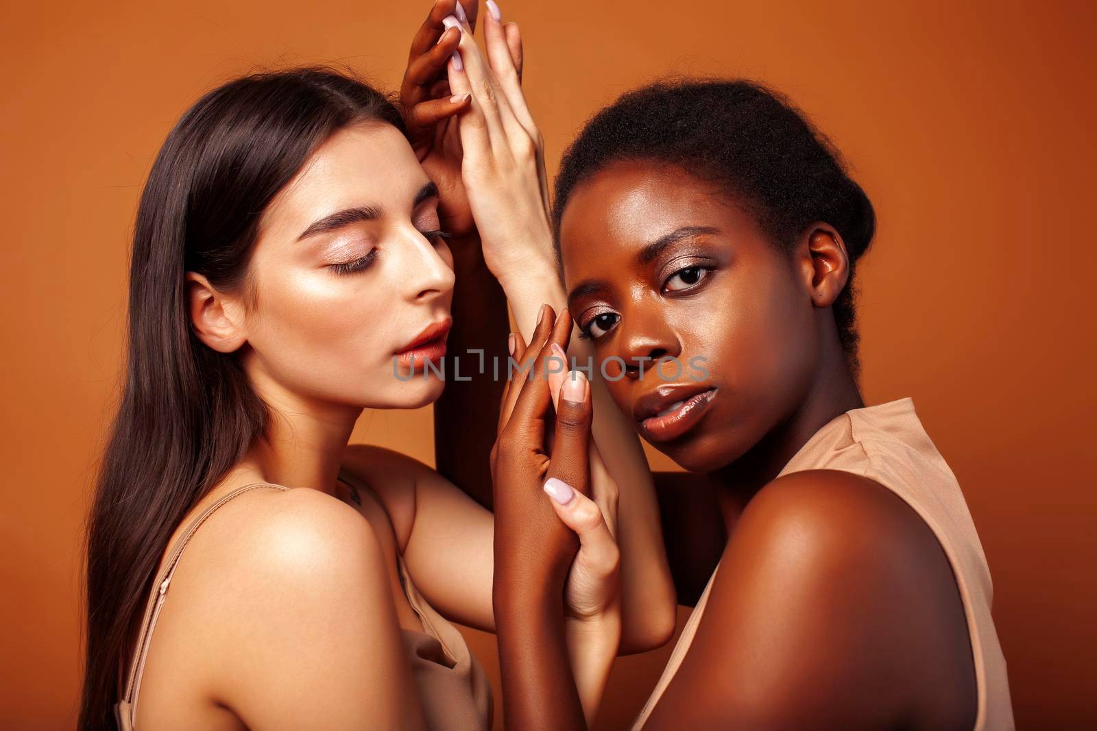 young pretty asian, afro woman posing cheerful together on brown background, lifestyle diverse nationality people concept close up