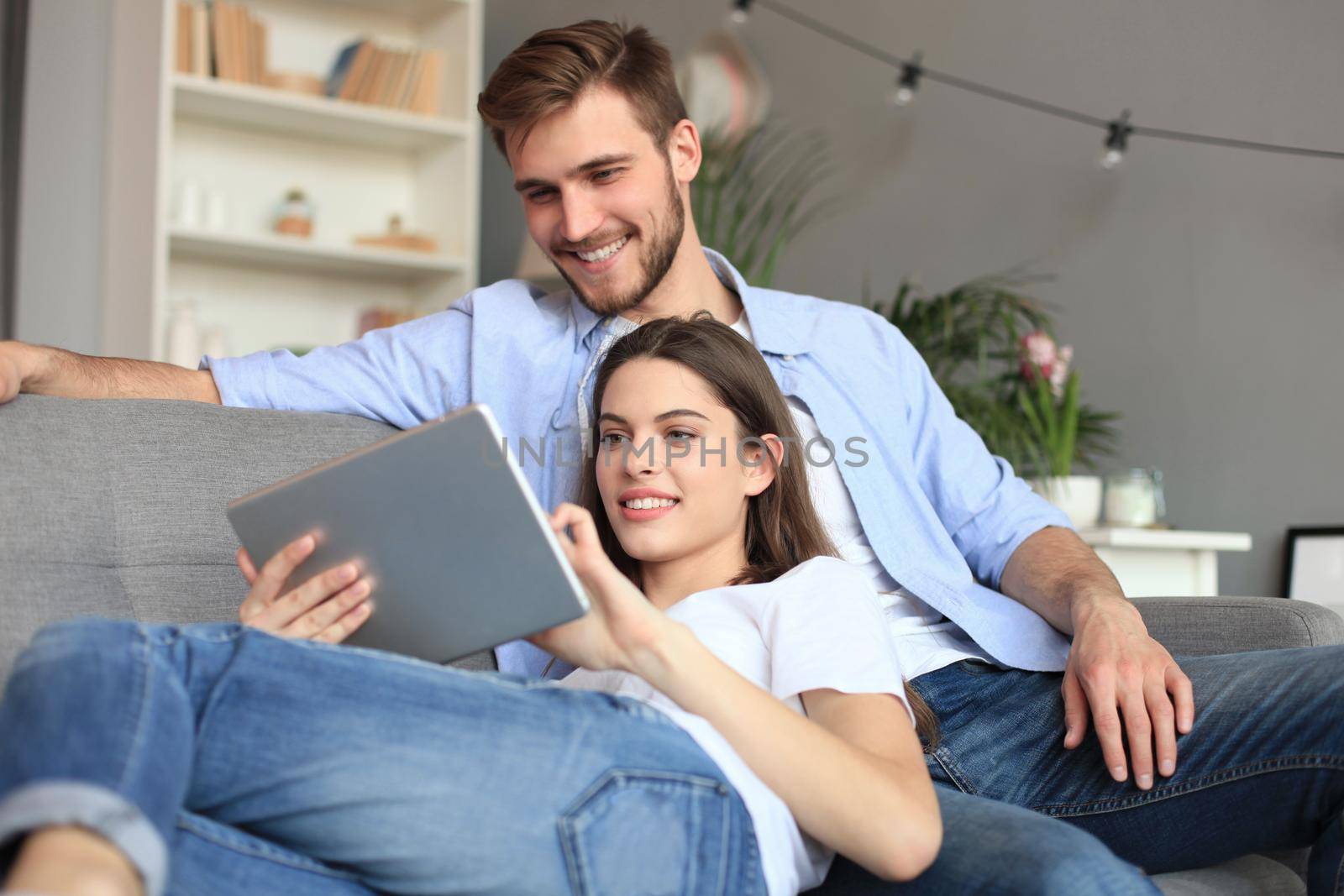 Young couple watching media content online in a tablet sitting on a sofa in the living room. by tsyhun