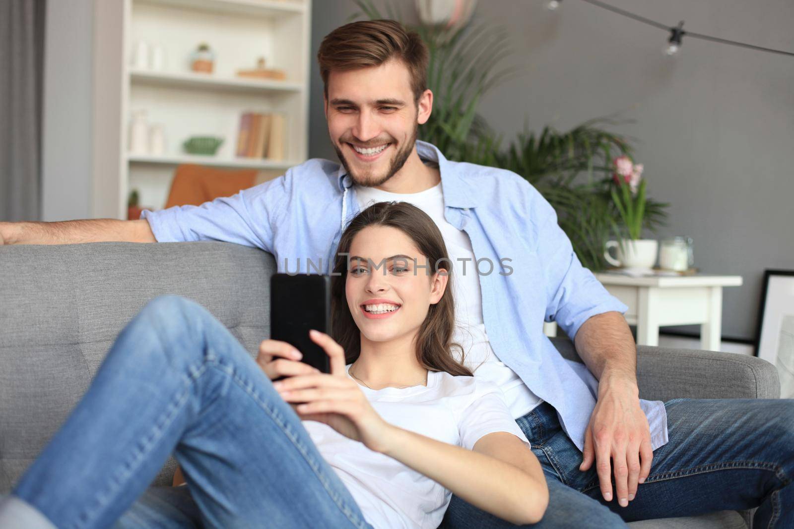 Young couple watching online content in a smart phone sitting on a sofa at home in the living room