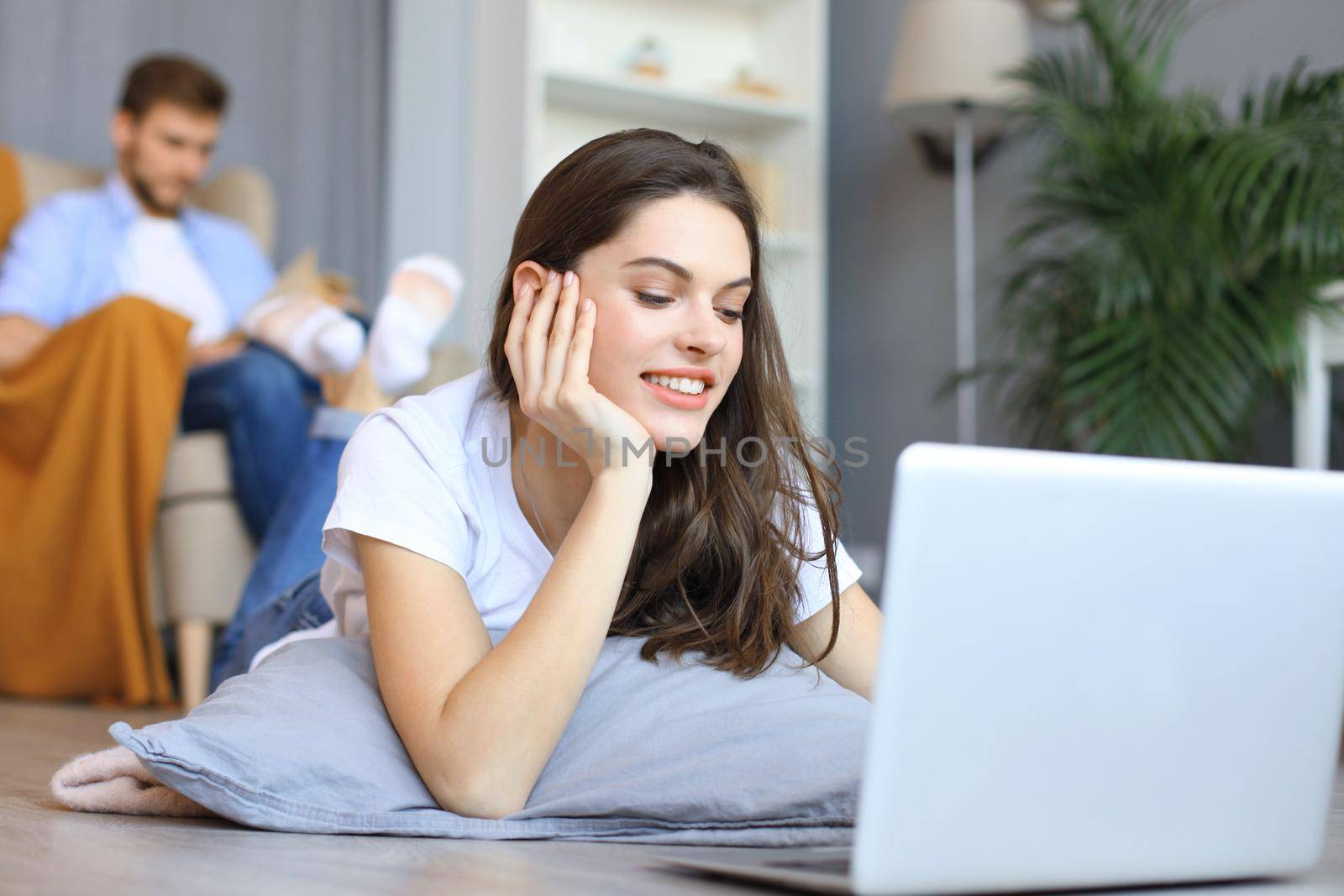 Smiling beautiful woman using laptop with blurred man in background at home. by tsyhun