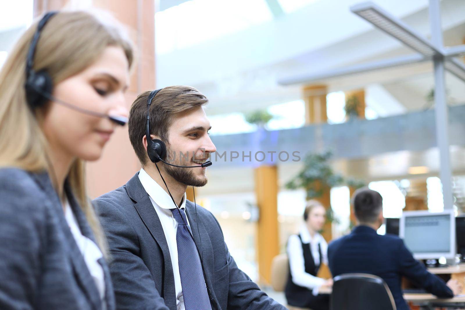 Portrait of call center worker accompanied by his team. Smiling customer support operator at work. by tsyhun