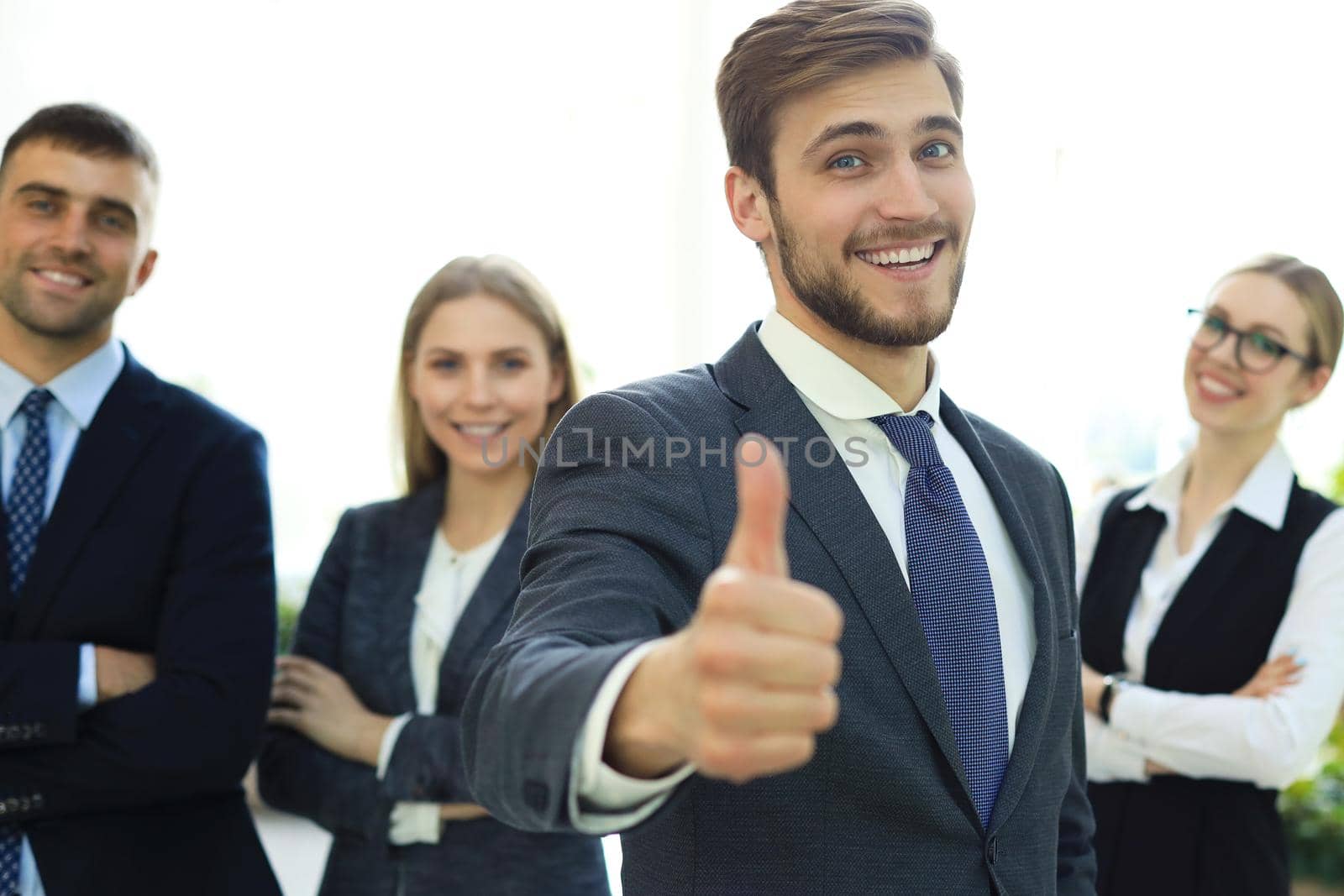 Happy businessman showing his thumb up and smiling while his colleagues standing in the background