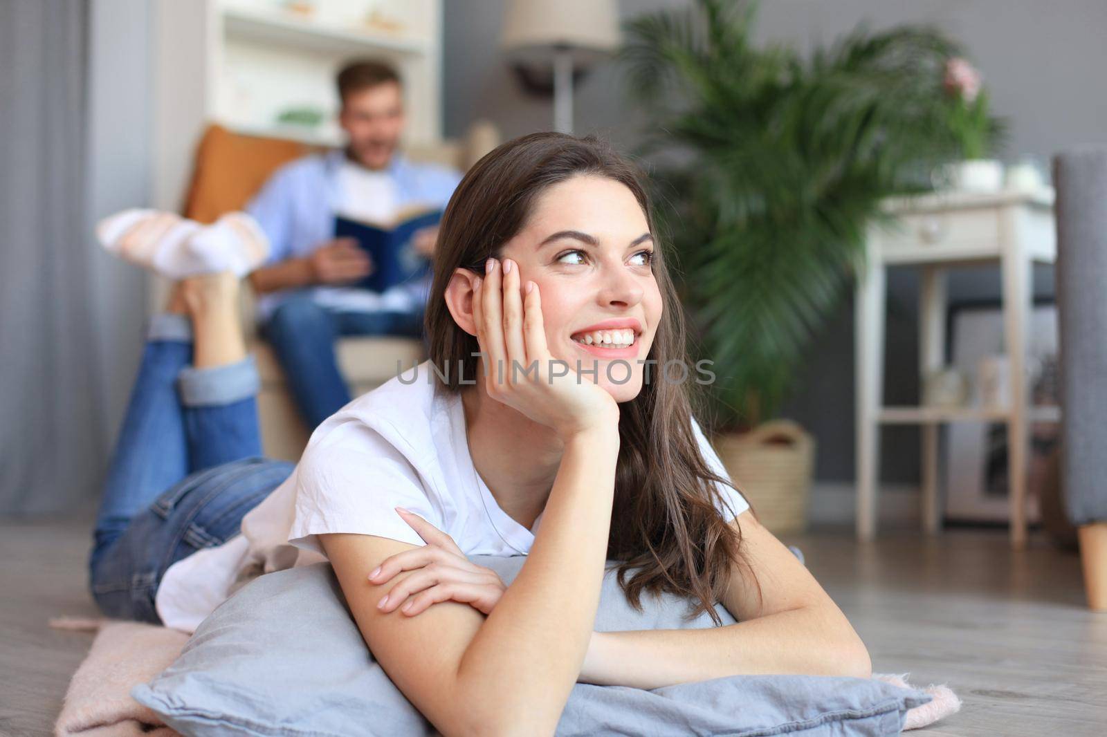 Portrait of attractive woman relaxing on floor with blurred man in background