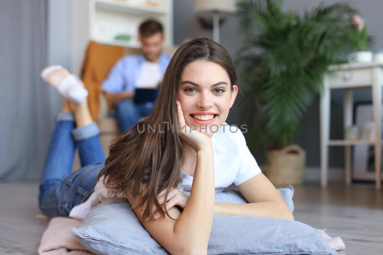 Portrait of attractive woman relaxing on floor with blurred man in background. by tsyhun