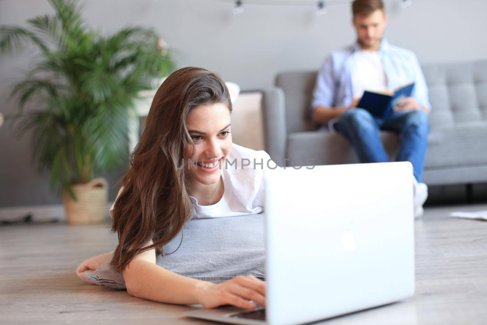 Smiling beautiful woman using laptop with blurred man in background at home. by tsyhun