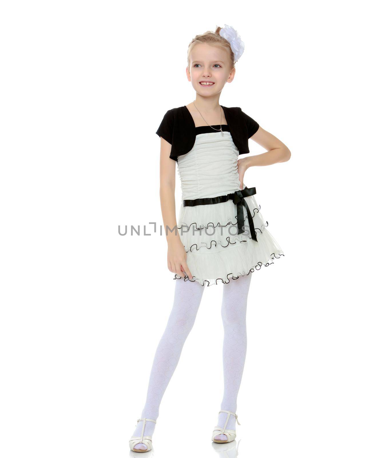 Beautiful little blonde girl dressed in a white short dress with black sleeves and a black belt.Girl poses for the camera.Isolated on white background.