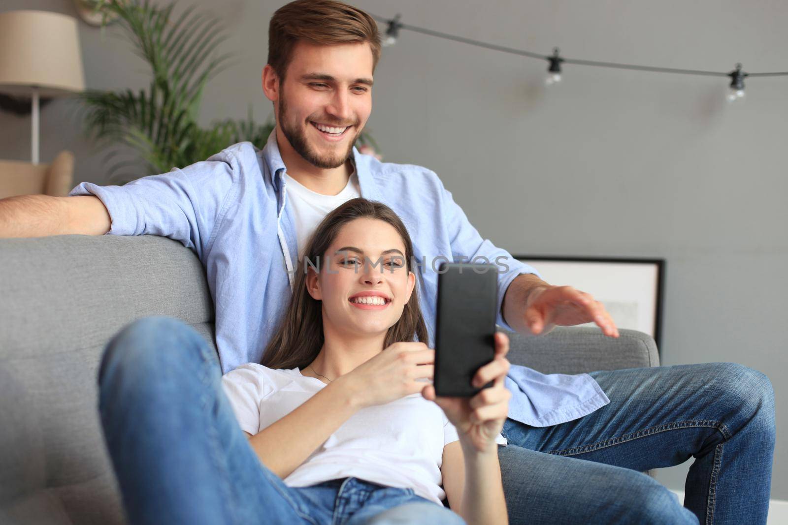 Young couple watching online content in a smart phone sitting on a sofa at home in the living room