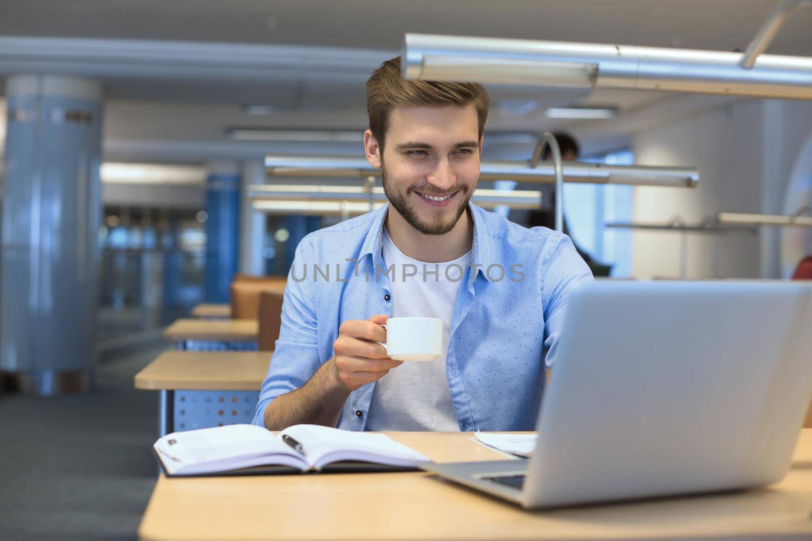 young man drinking coffee in office while typing on laptop