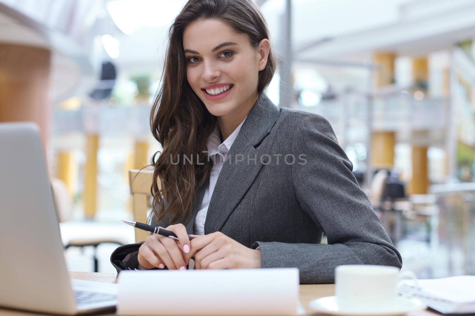 Portrait of a cheerful young businesswoman sitting at the table in office and looking at camera