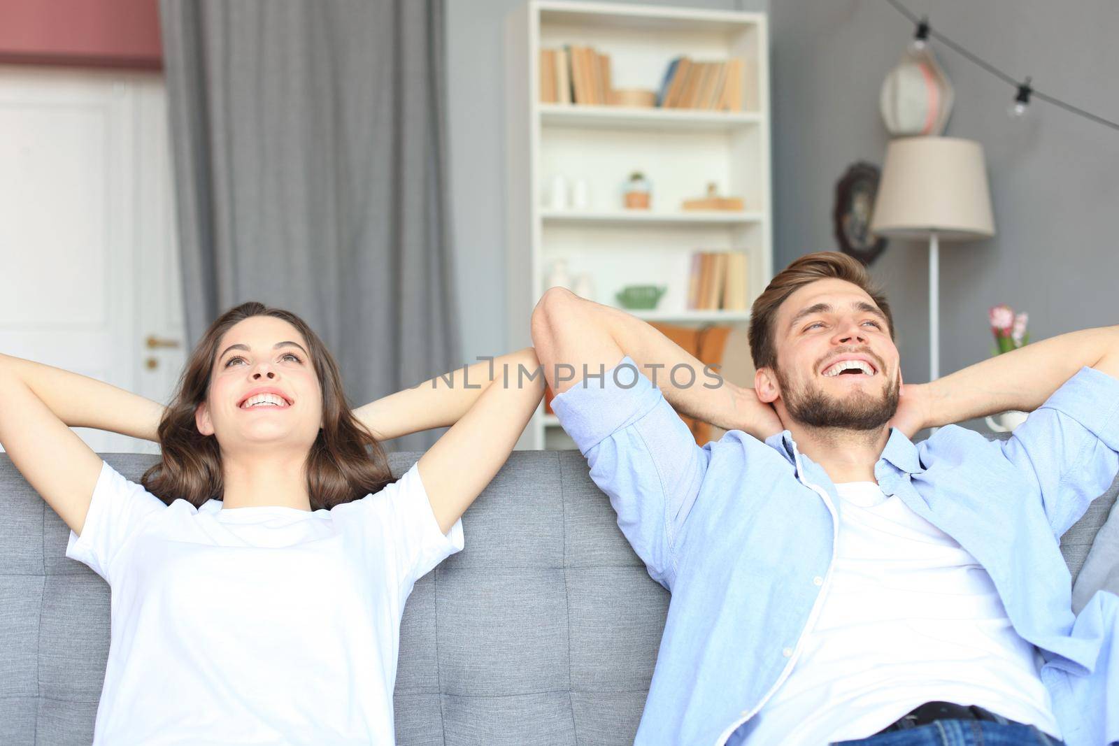 Smiling beautiful couple sitting on a sofa and dreaming about new home. by tsyhun