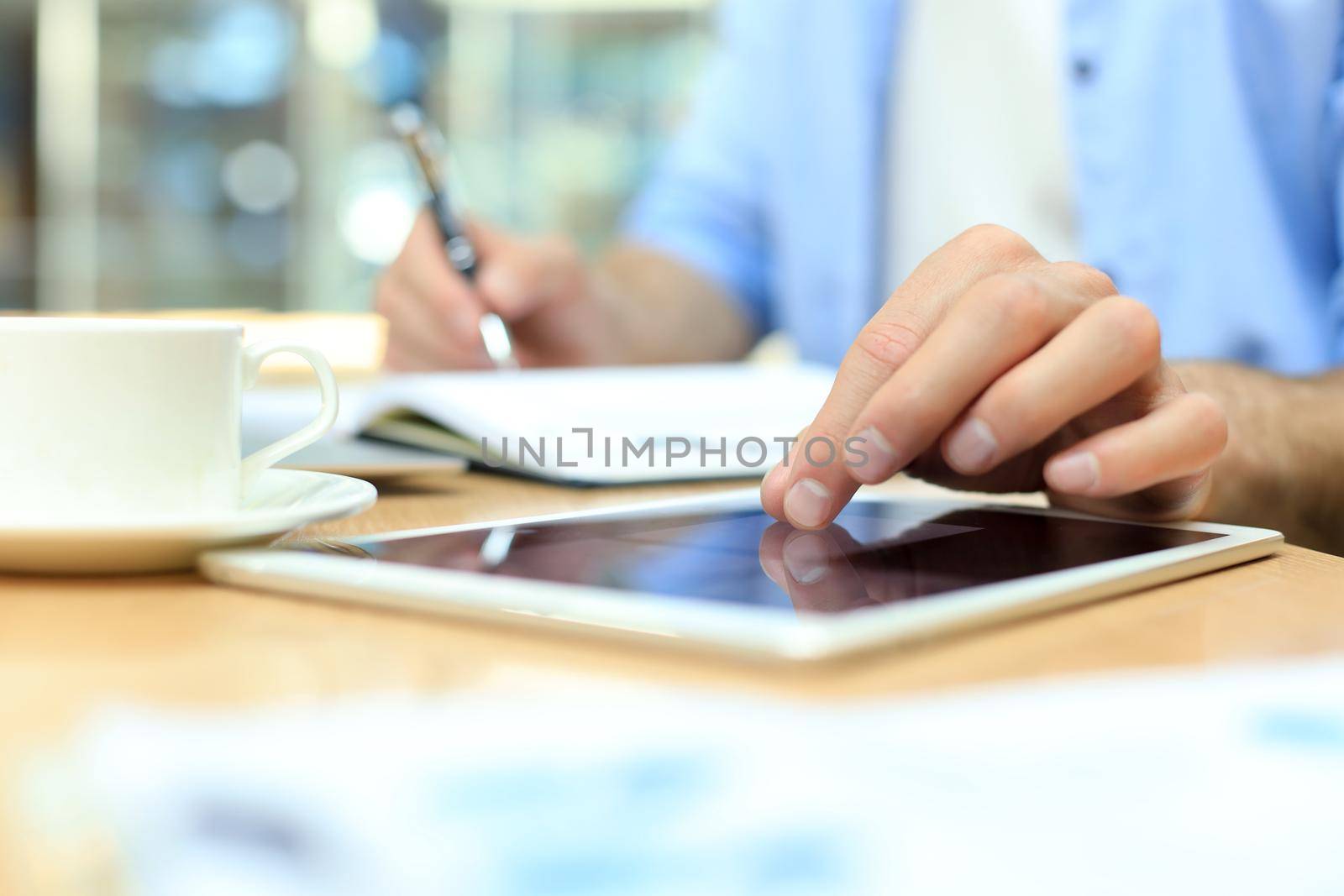 Man writing work plan with pen on paper notebook, browsing internet on digital tablet on office desk