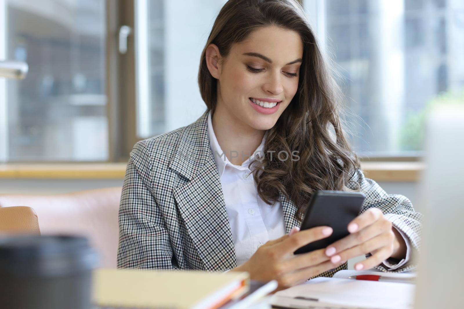 Young smiling business woman using smartphone near computer in office