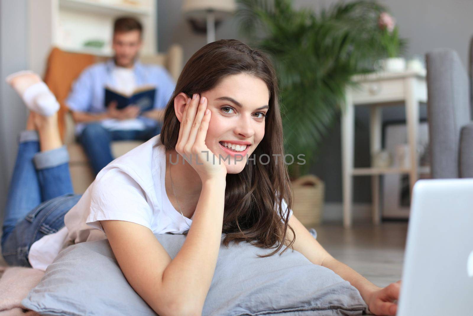 Smiling beautiful woman using laptop with blurred man in background at home