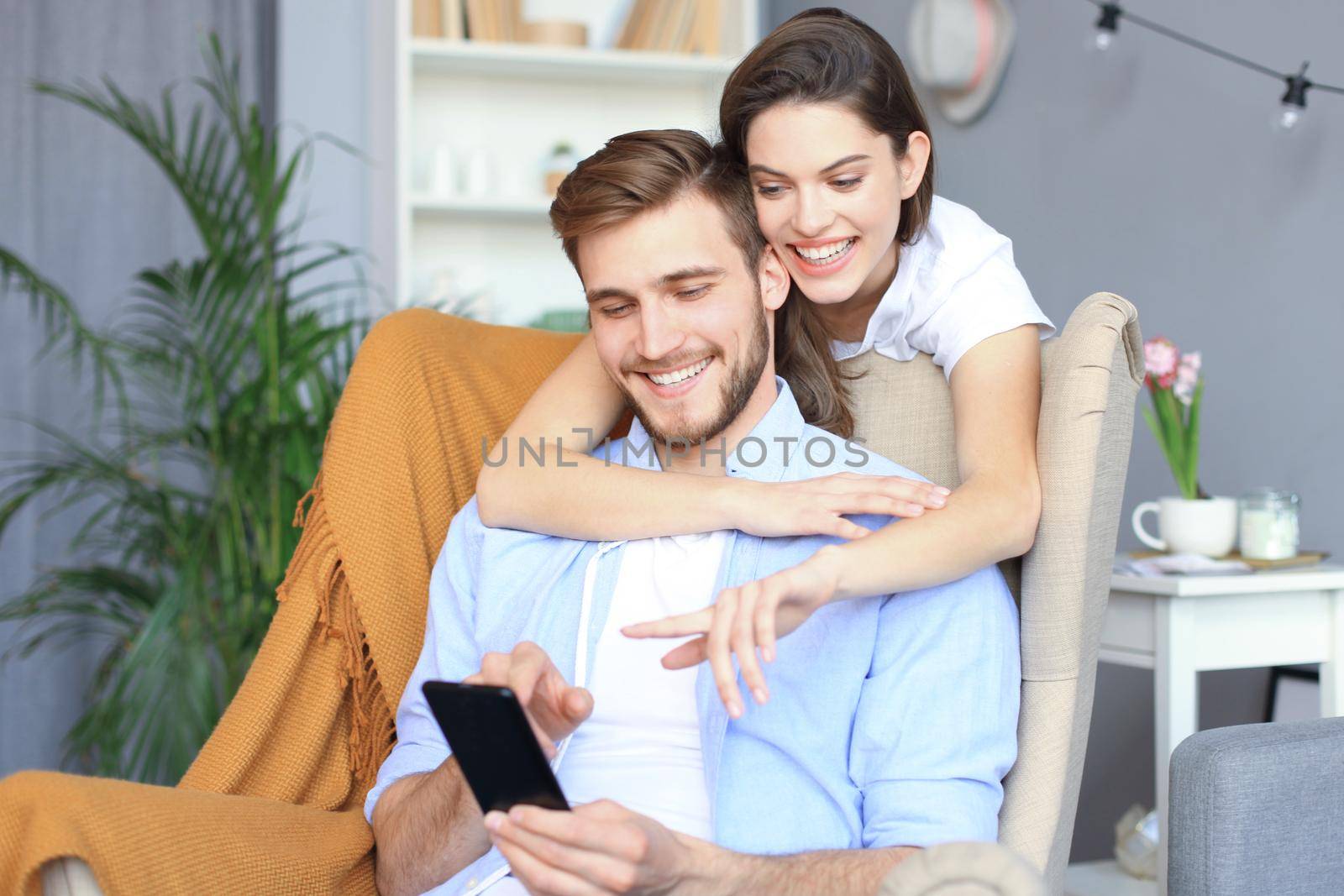 Young couple watching online content in a smart phone sitting on chair at home in the living room