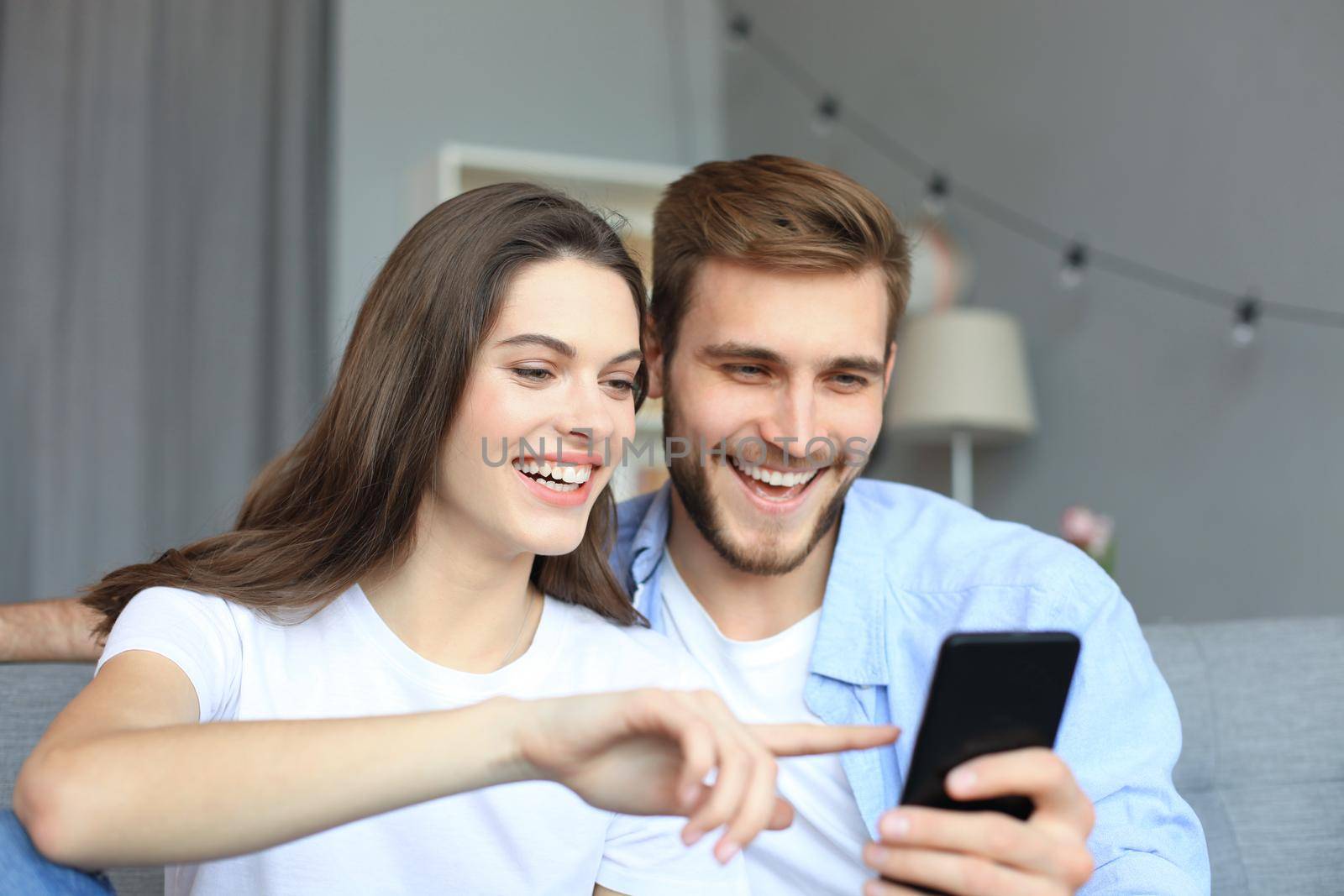 Young couple watching online content in a smart phone sitting on a sofa at home in the living room. by tsyhun