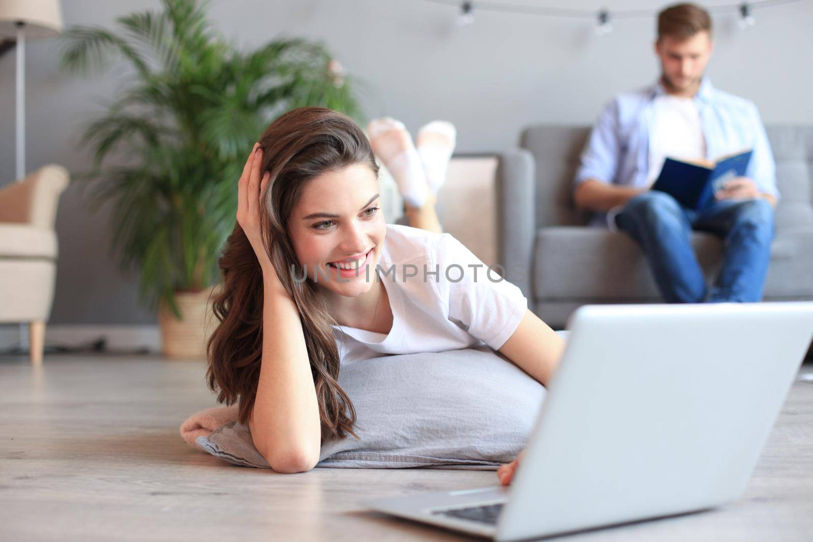 Smiling beautiful woman using laptop with blurred man in background at home. by tsyhun