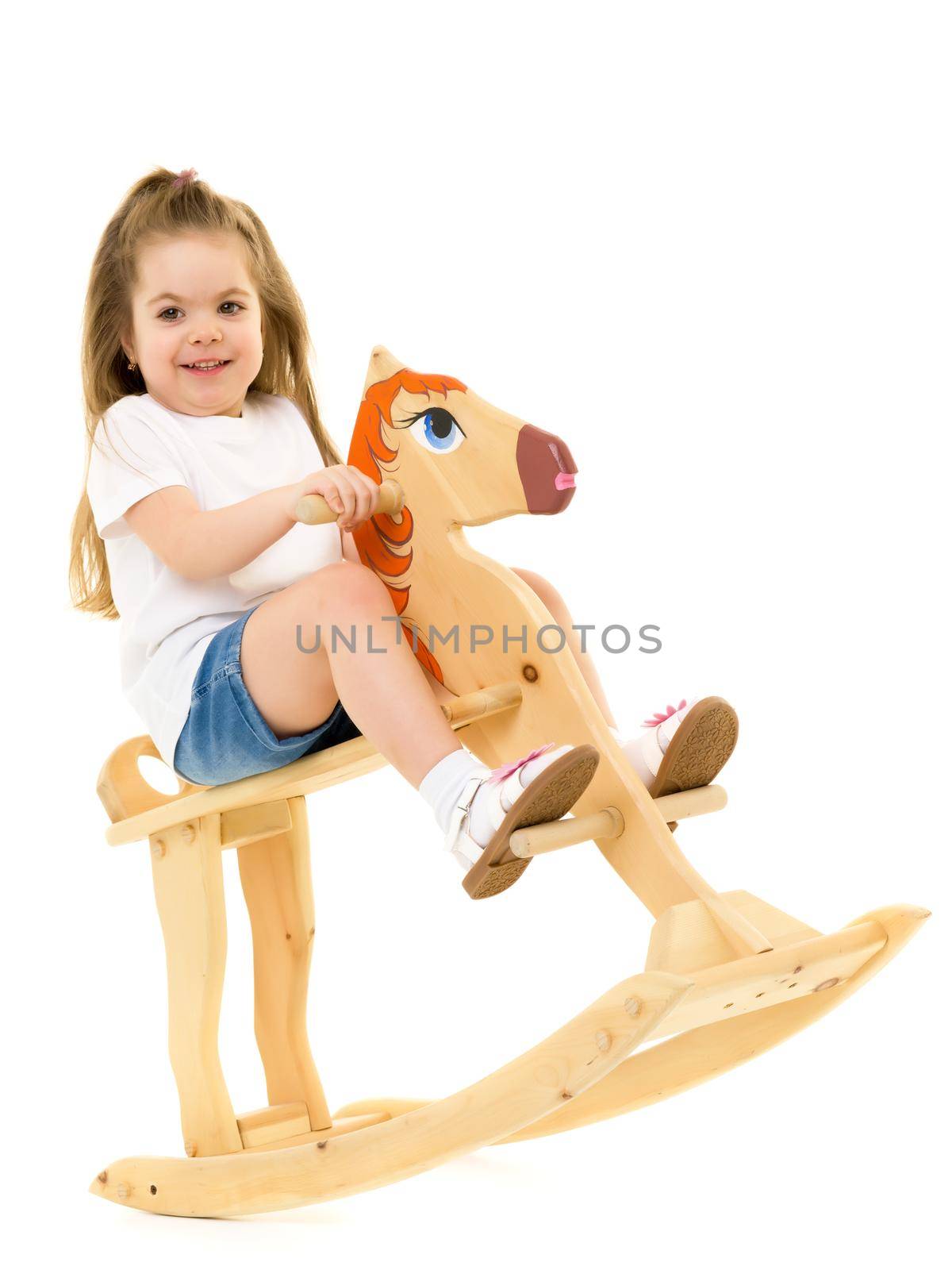 Little girl swinging on a wooden horse. The concept of a happy childhood, games in kindergarten and in the family. Isolated against white background.