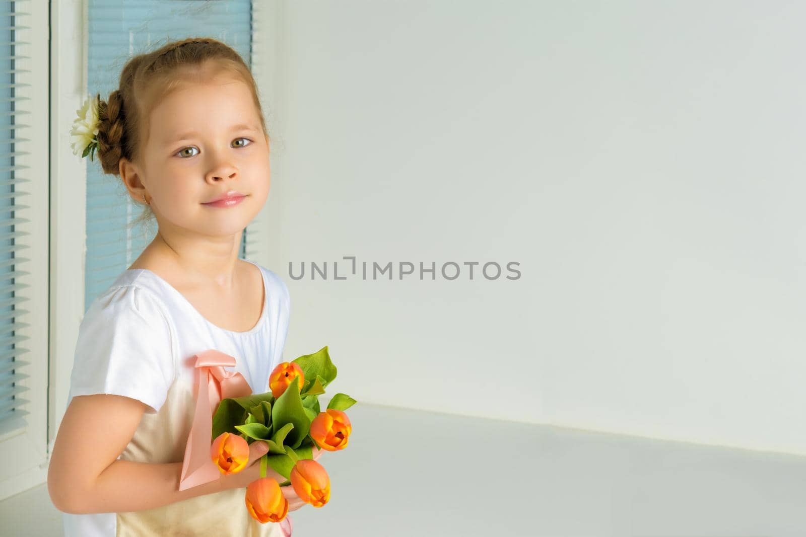 A nice little girl sits on a window sill with a bouquet of tulips. The concept of happy people, spring vacation.