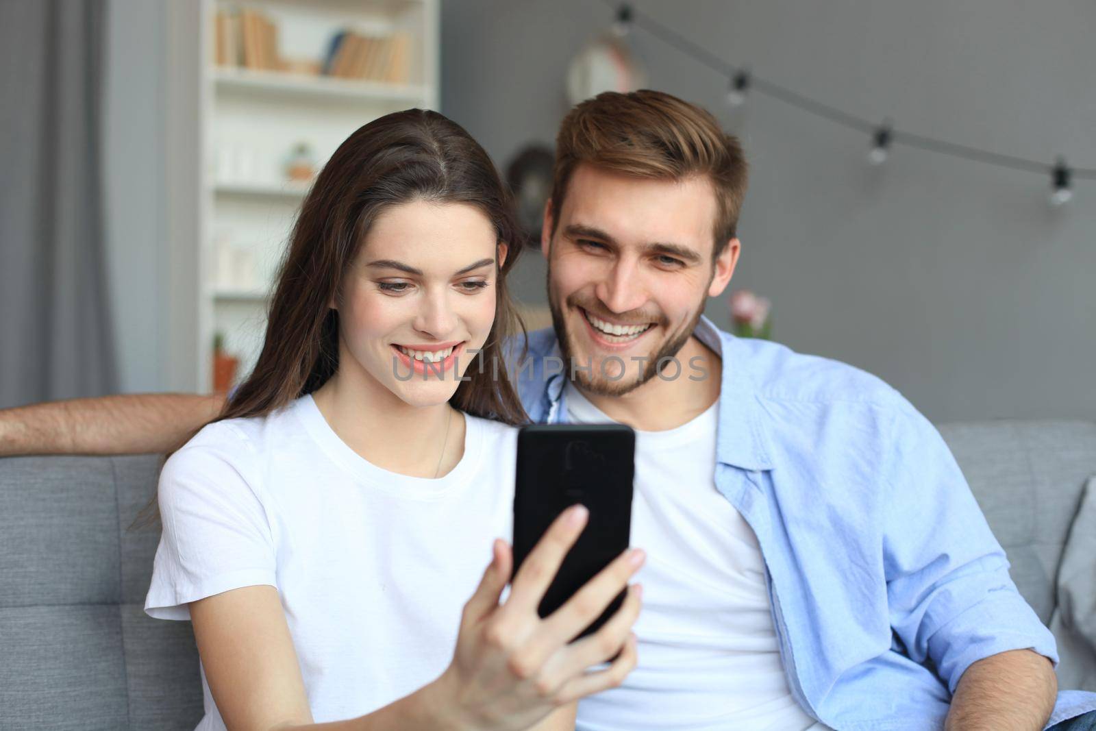 Young couple watching online content in a smart phone sitting on a sofa at home in the living room