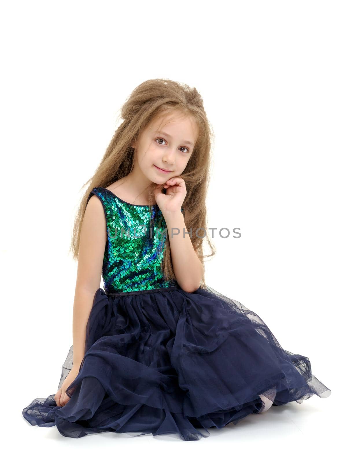 Beautiful little girl is sitting on the floor in the studio. The concept of a happy childhood, beauty and fashion. Isolated on white background.