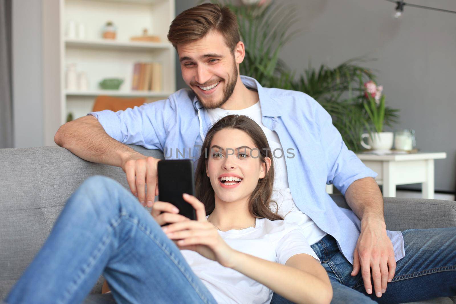 Young couple watching online content in a smart phone sitting on a sofa at home in the living room. by tsyhun