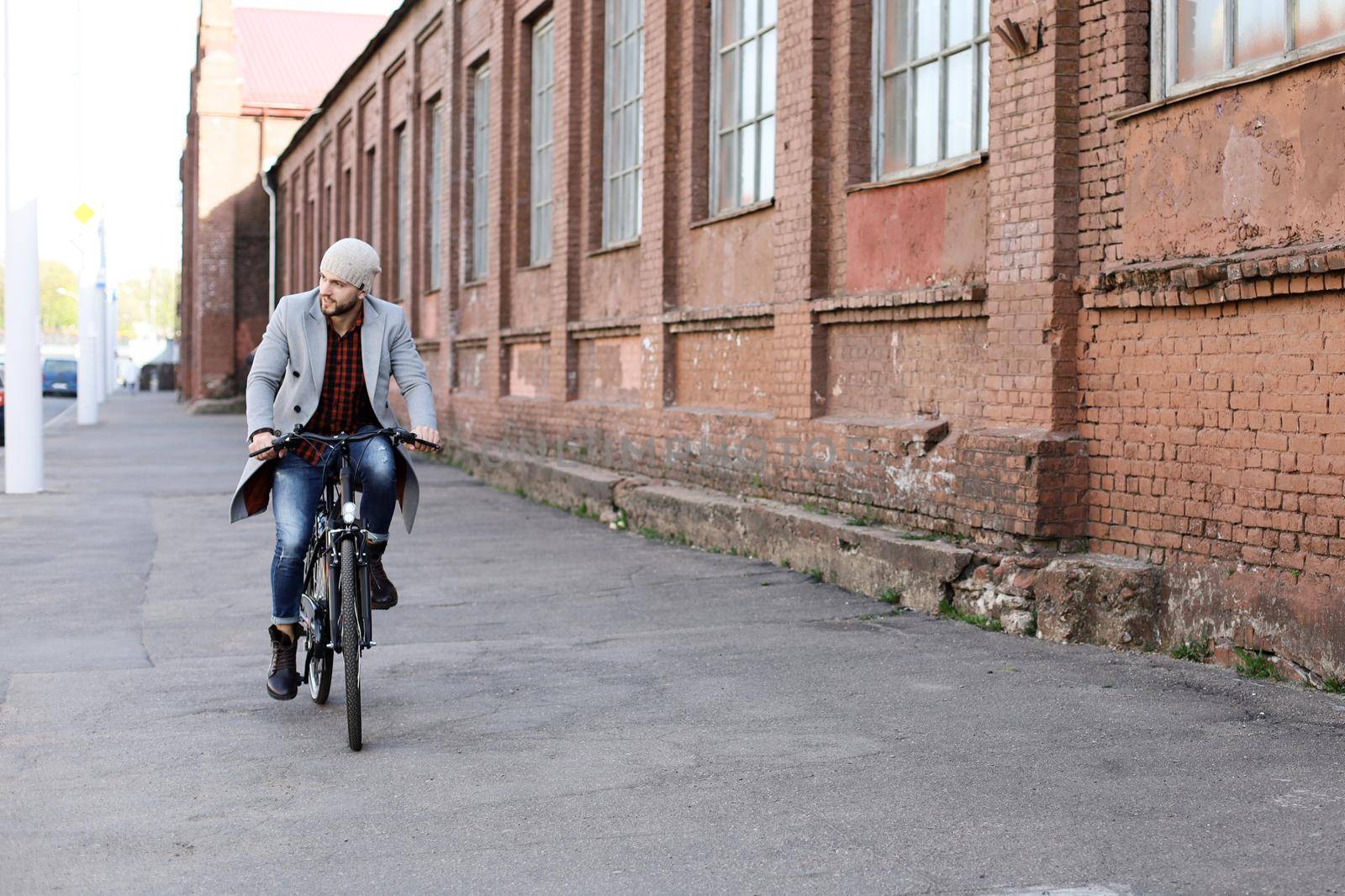 Handsome young man in grey coat and hat riding a bicycle street in the city