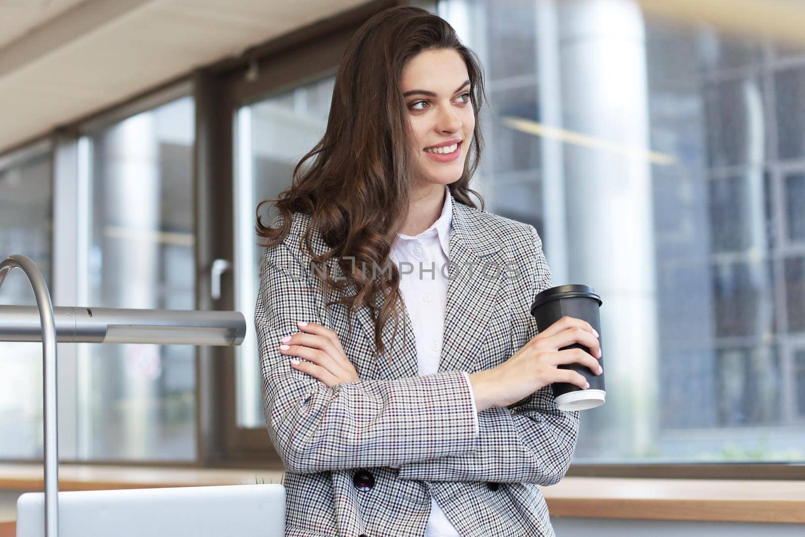 Attractive smiling businesswoman standing in the office with a cup of coffee
