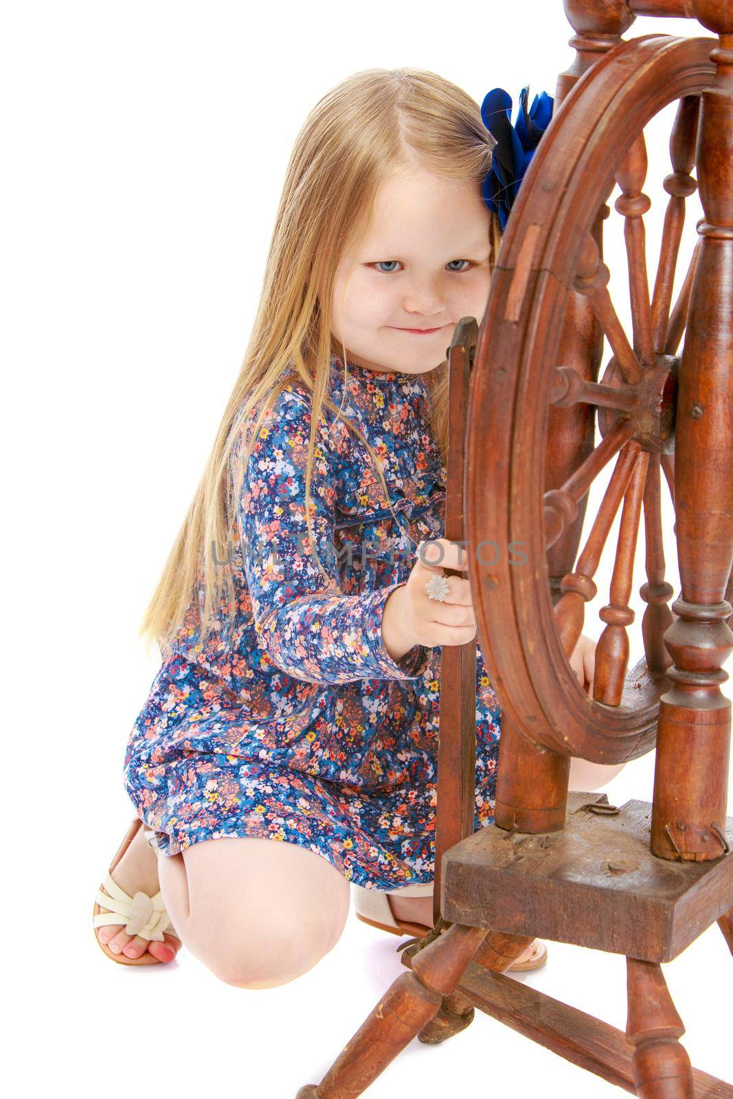 Curious little girl with long blond hair below the shoulders,which are attached to a large blue flower . The girl enthusiastically looking at the old spinning wheel - Isolated on white background