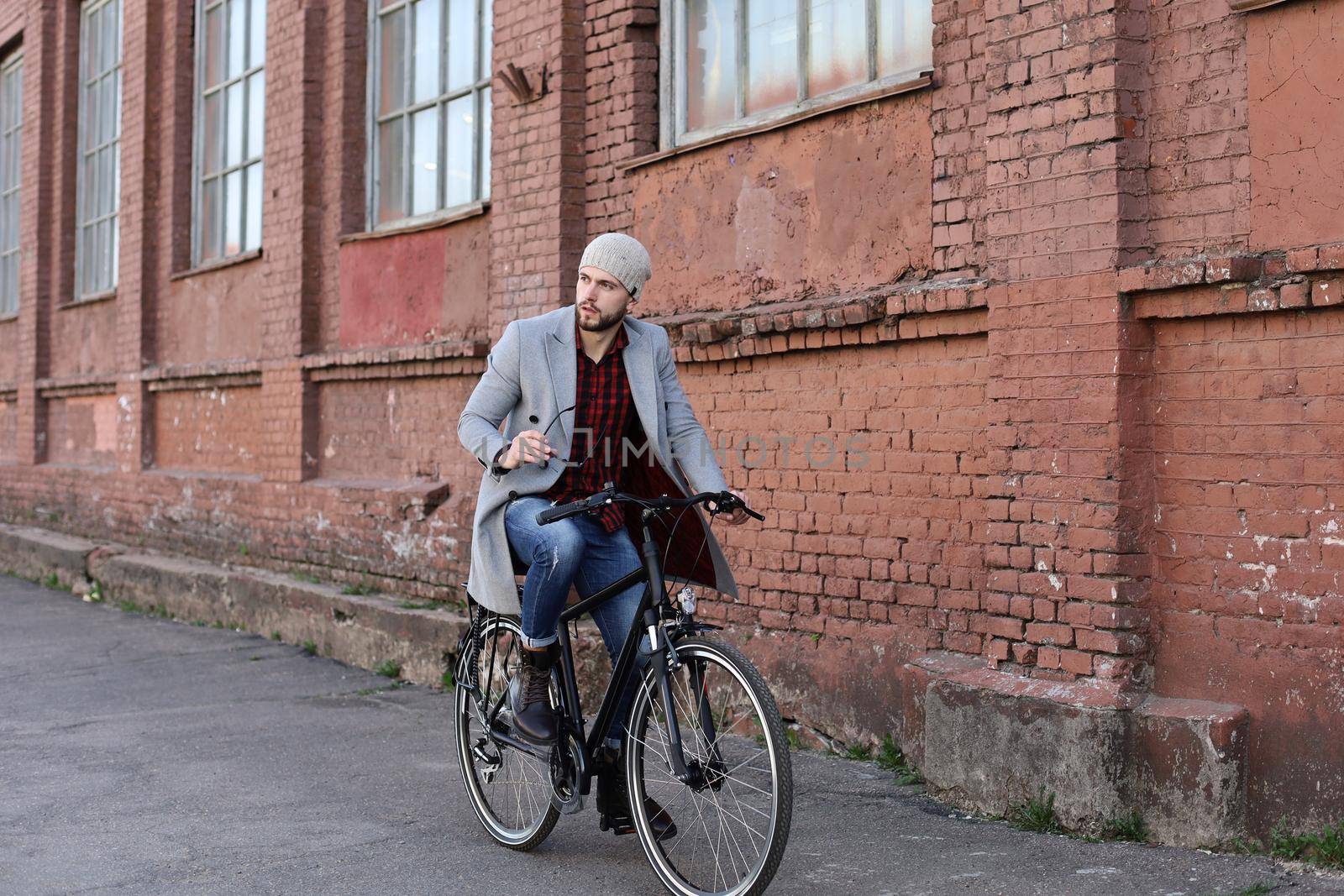 Handsome young man in grey coat and hat riding a bicycle street in the city