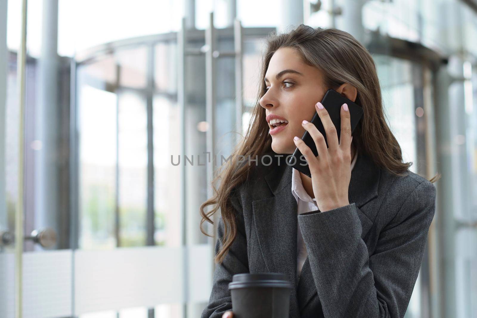 Young smiling business woman using smartphone near computer in office