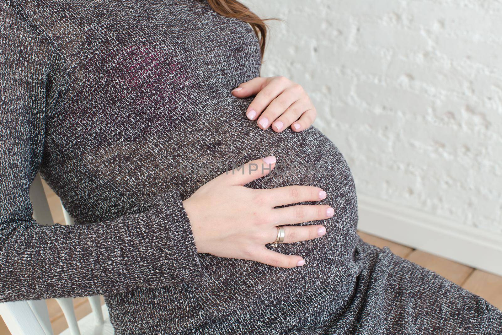 Pregnant female's belly. Studio shot. Female wearing grey knitted dress.