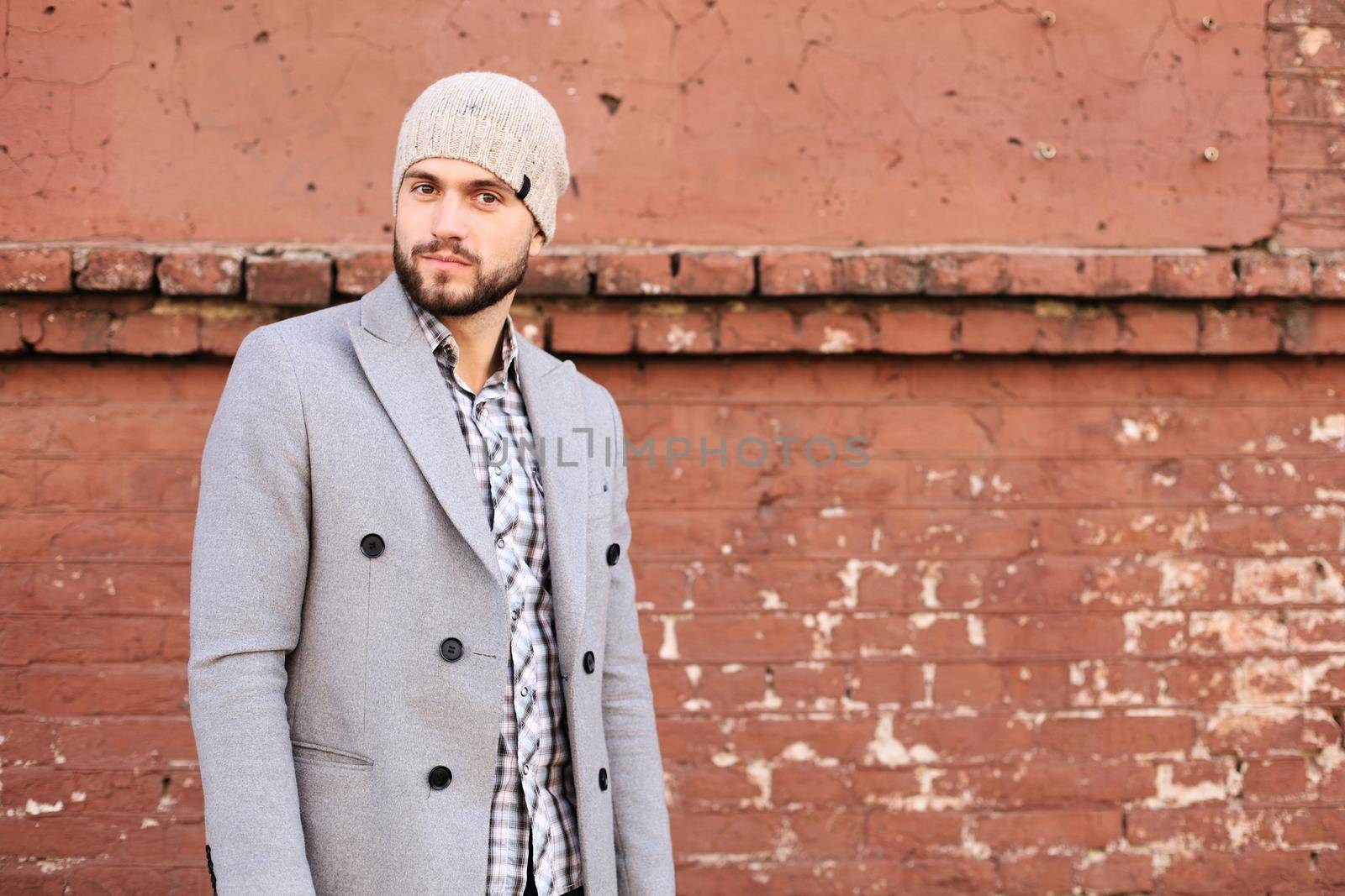 City life. Stylish young man in grey coat and hat standing on the street in the city