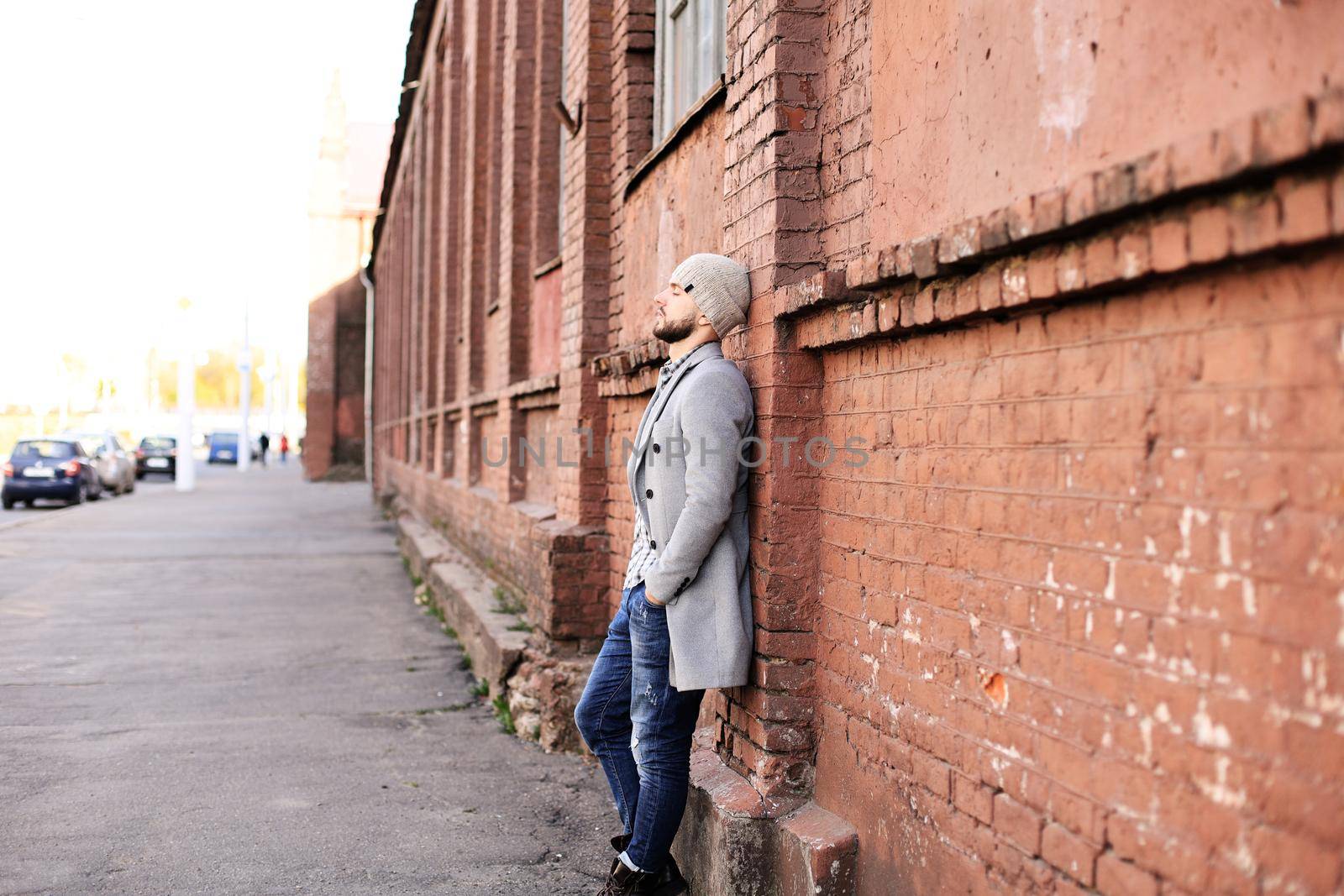 City life. Stylish young man in grey coat and hat standing on the street in the city