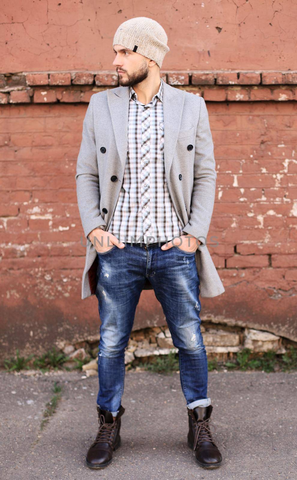 City life. Stylish young man in grey coat and hat standing on the street in the city