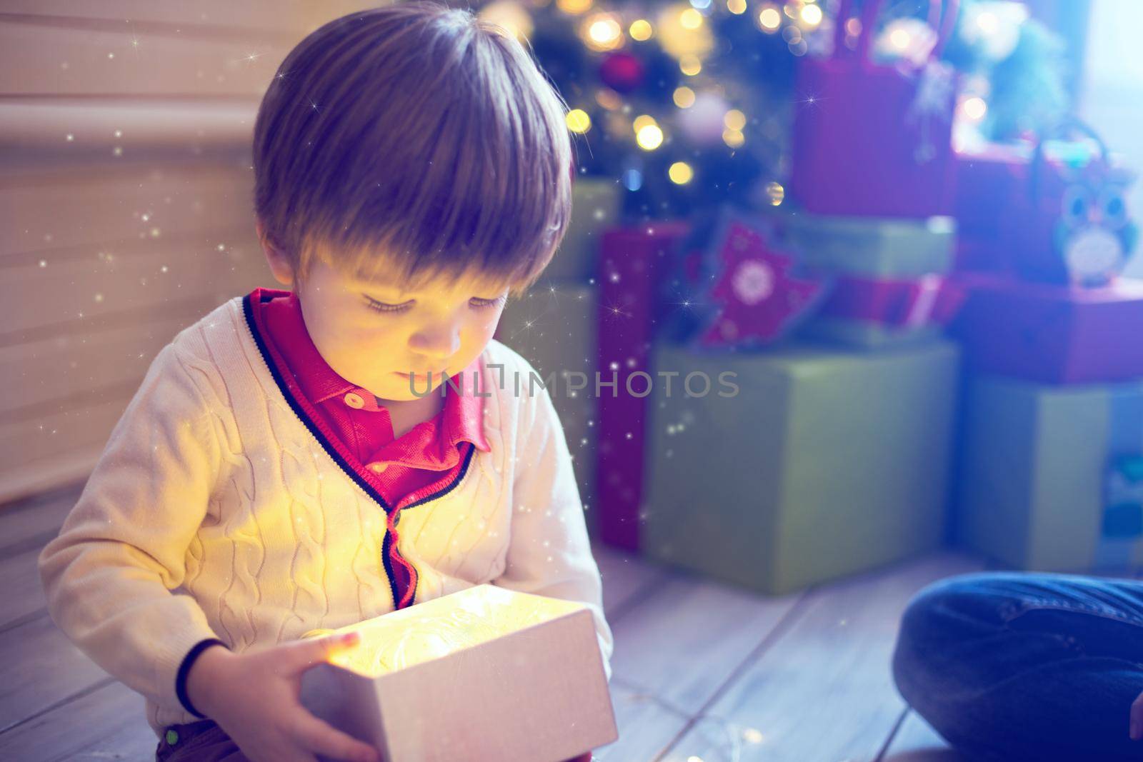 Surprised child opening and looking inside a magic gift over Christmas tree.