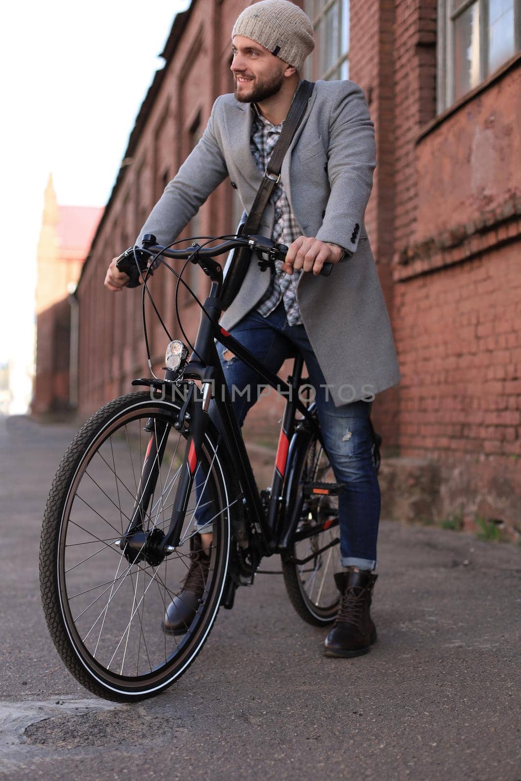 Handsome young man in grey coat and hat standing with his bicycle