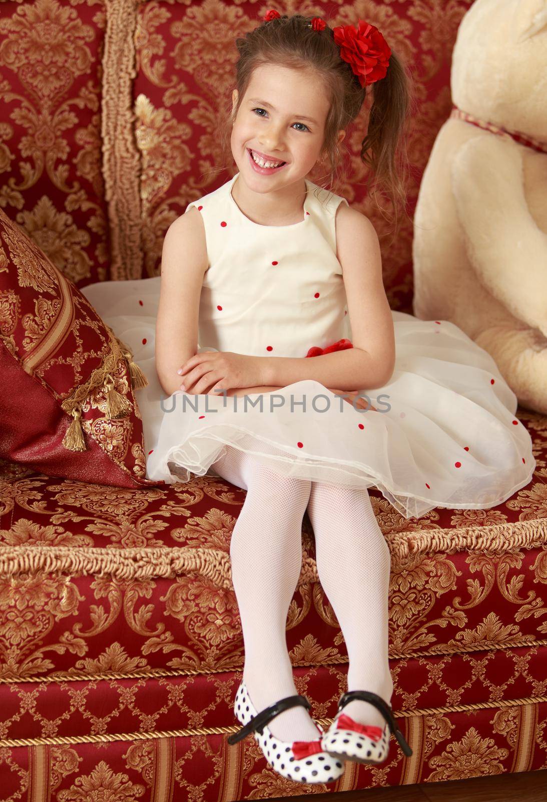 Cute little girl in smart white dress is sitting on a luxury sofa Persian