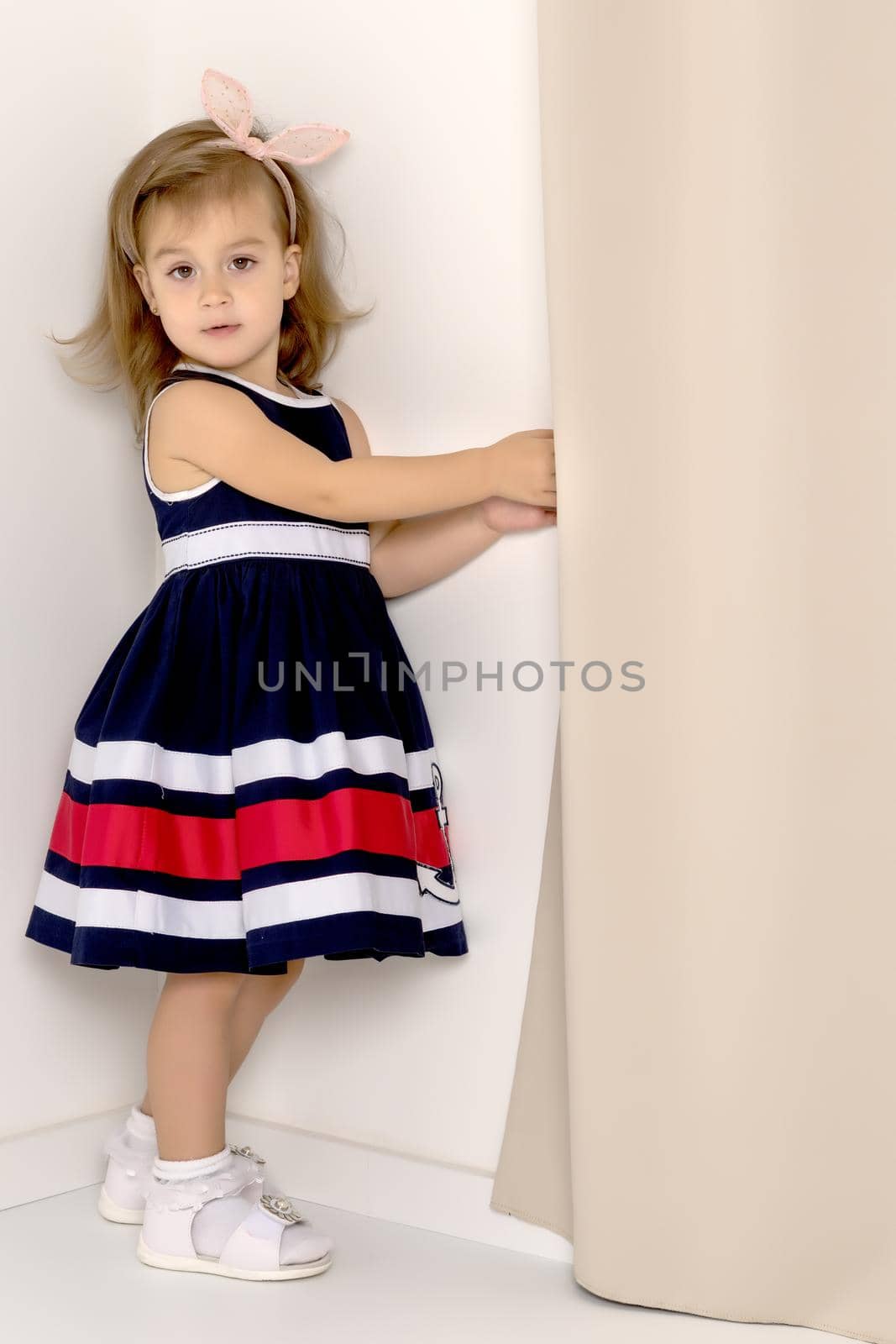 Cute little girl peeks behind the curtains. The concept of home comfort, happy childhood.
