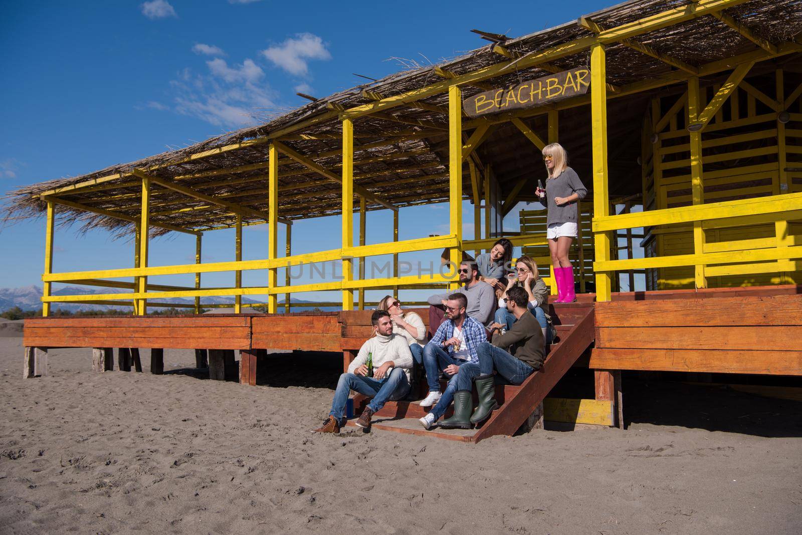 Happy Group Of Friends Hanging Out At Beach House having fun and drinking beer on autumn day