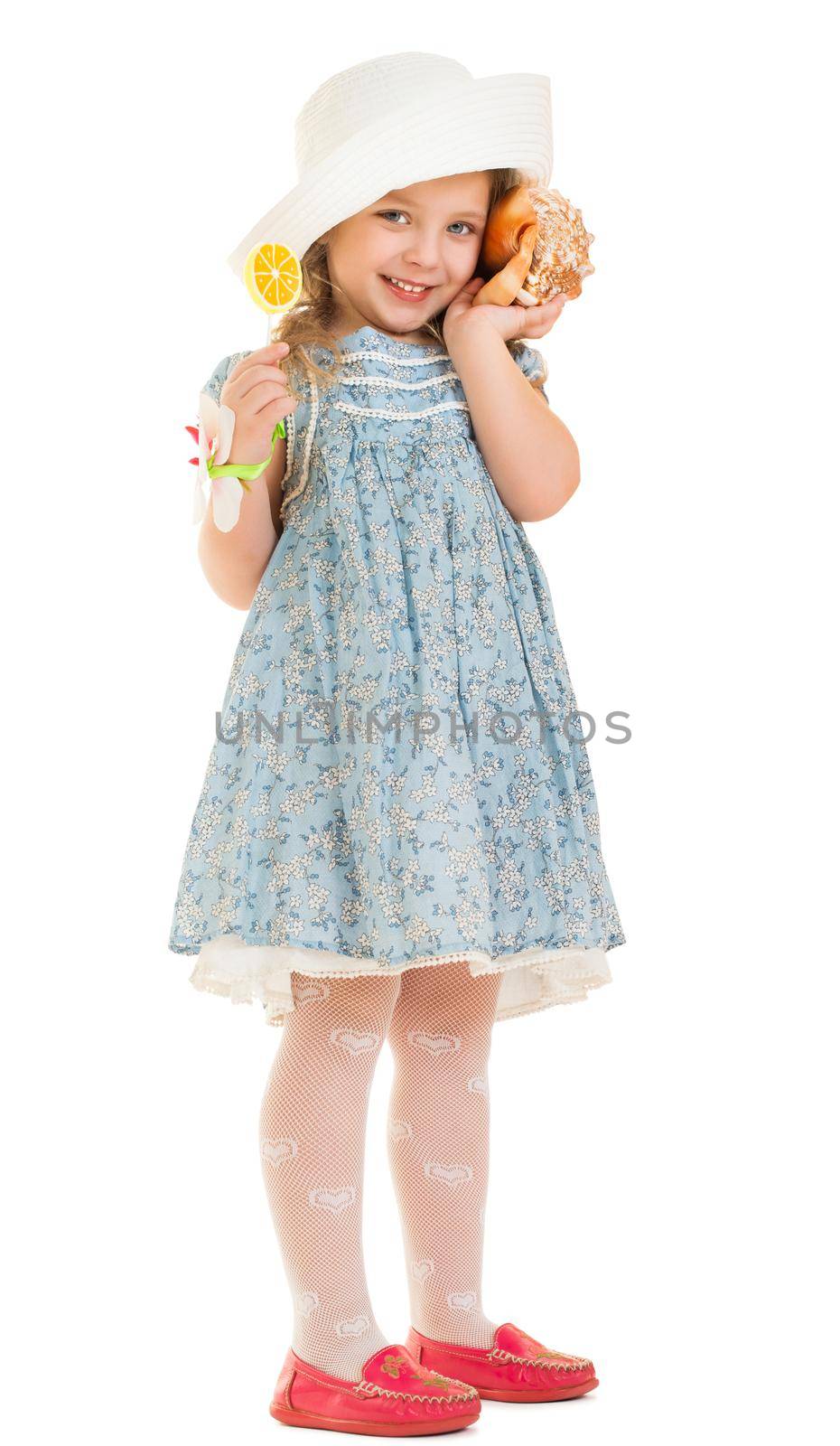 Cute little girl in a blue short dress and white hat attached to the ear a large sink . The girl listens to the sound of the sea-Isolated on white background