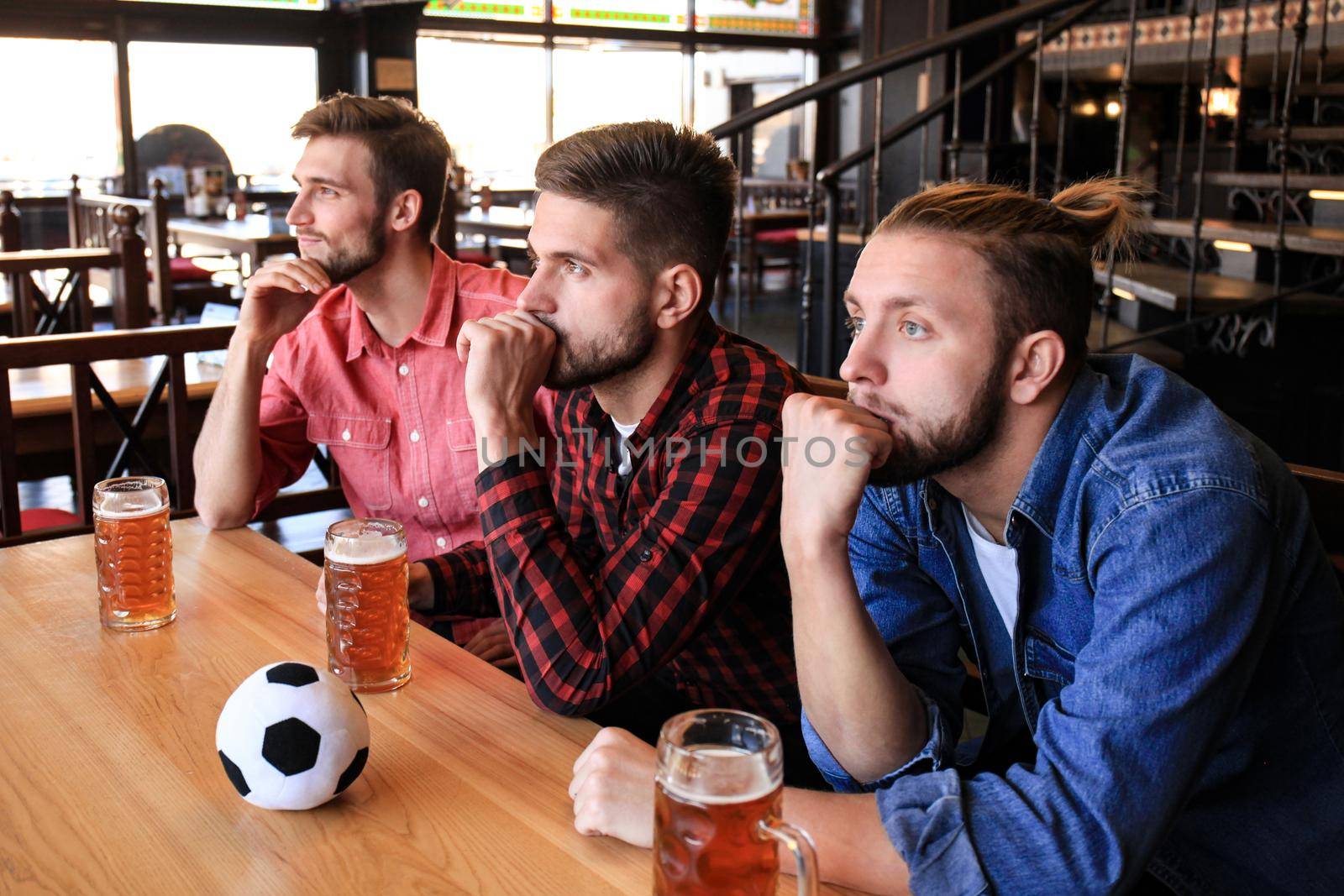 Sad male football fans watching game at bar and drinking beer