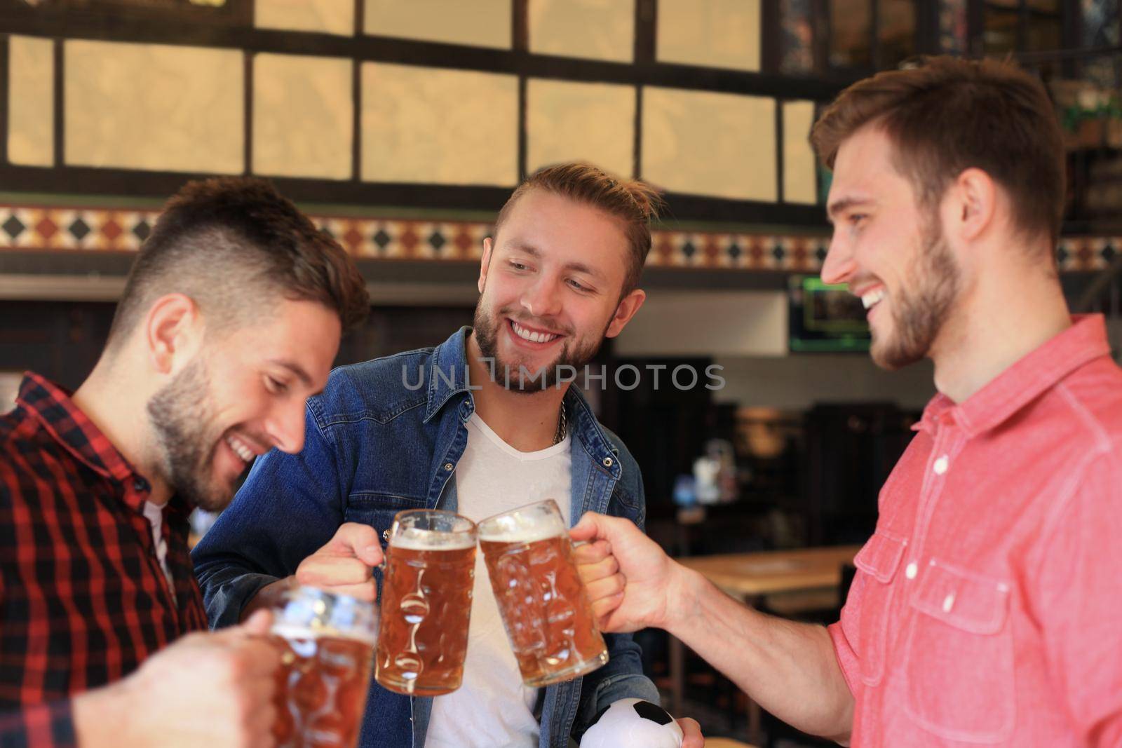 Cheerful old friends having fun and drinking draft beer at bar counter in pub